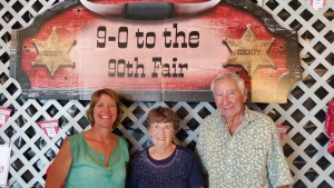 Janelle Hansen of Hemingford was named a 2015 Good Neighbor during the Box Butte County Fair. With the fair theme “9-0 to the 90th Fair” as a backdrop, she is shown with Ak-Sar-Ben Ambassadors Betty and Arlee Phillips. (Photo courtesy of Mary Crawford)